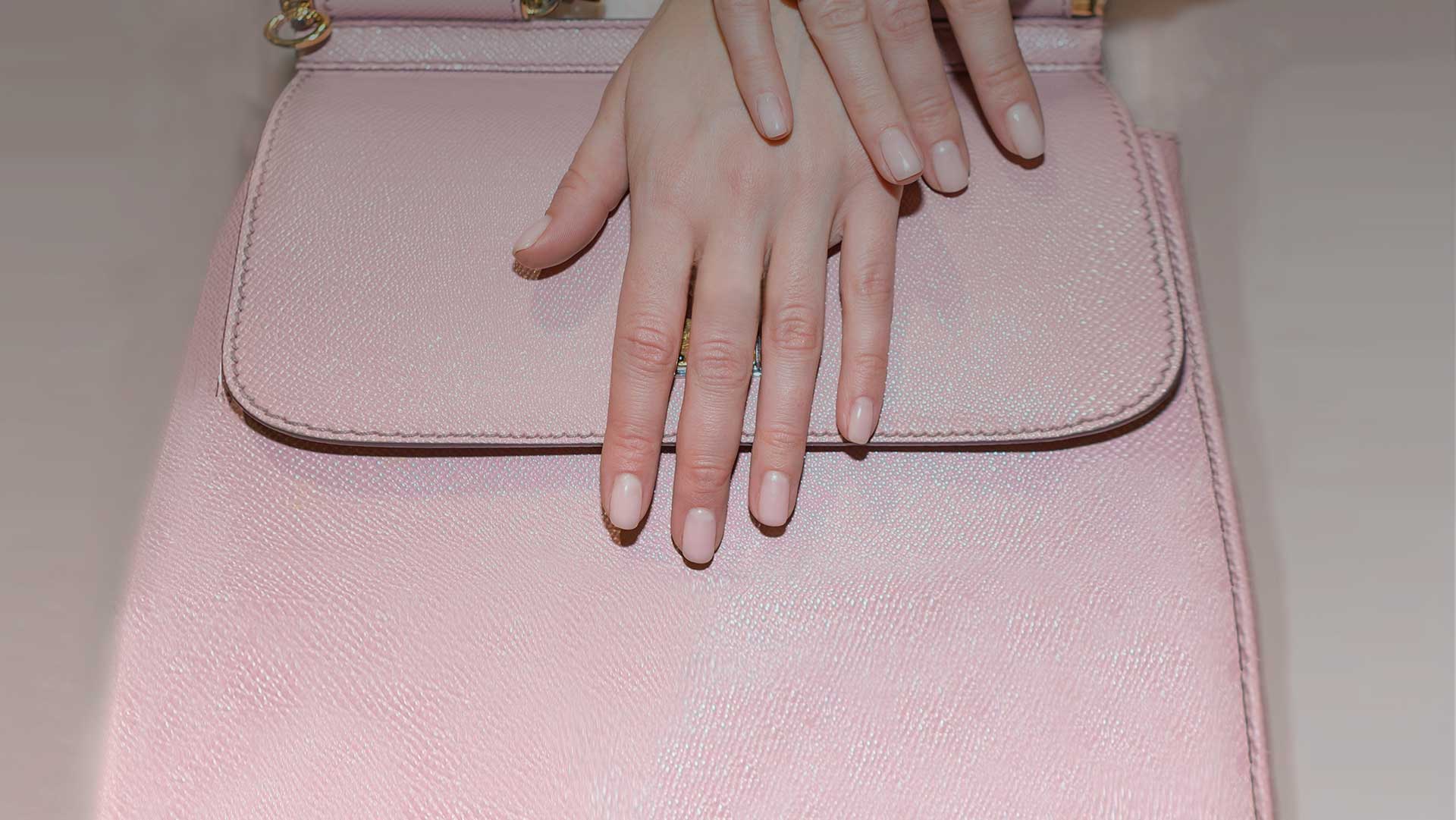 Elegant hands with pink manicured nails on luxurious pink leather background